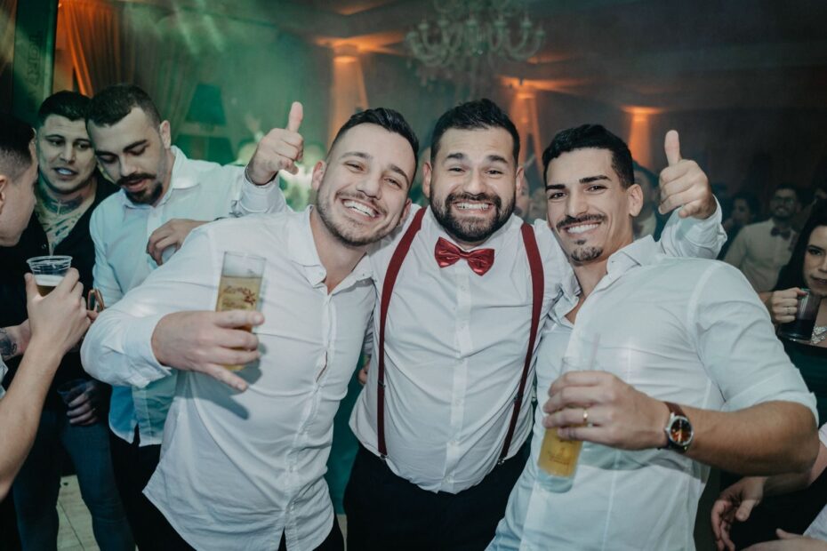 A group of happy adult men enjoying drinks and cheering at an indoor party.